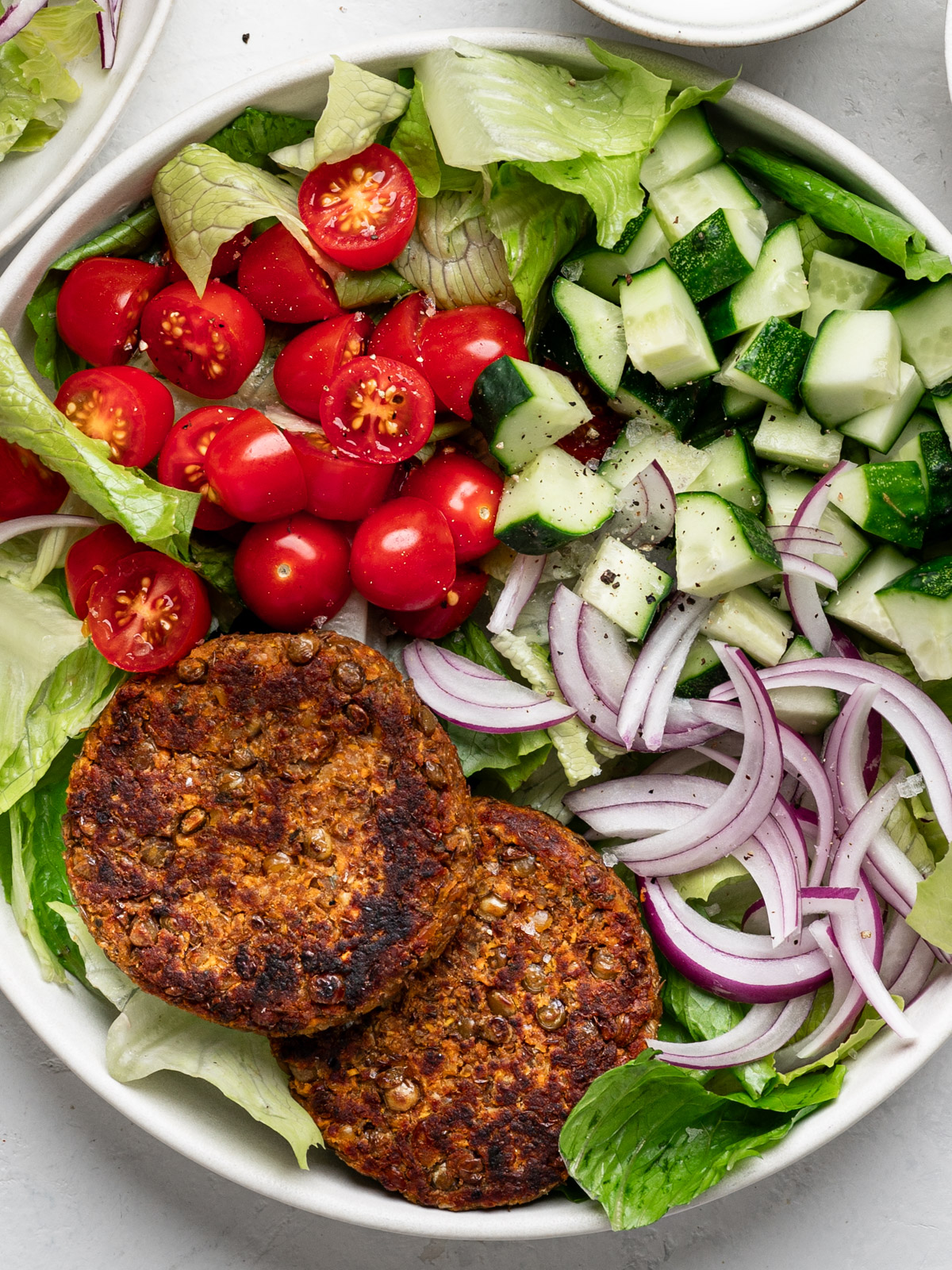lentil patties served on a plate with salad greens with tomatoes, onions and cucumbers