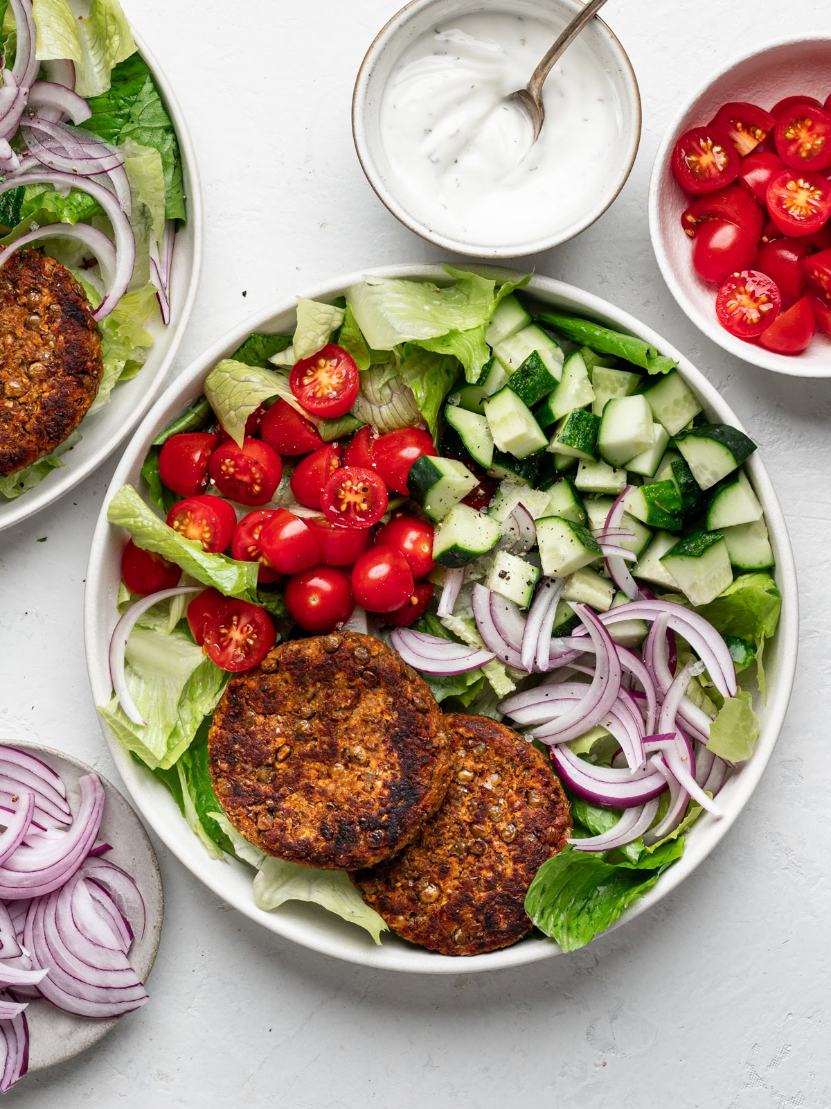 lentil patties served on two plates with salad greens, tomatoes, onions and cucumbers and dipping sauce on the side