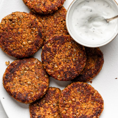 lentil patties on a white platter with yogurt dipping sauce in a small bowl on the side