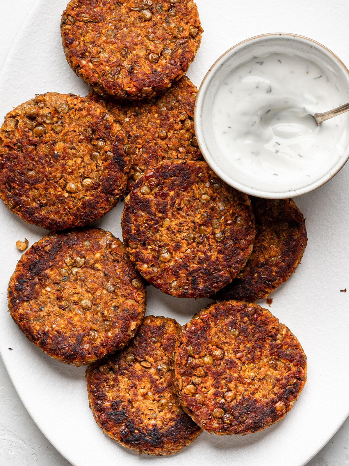 lentil patties on a white platter with yogurt dipping sauce in a small bowl on the side