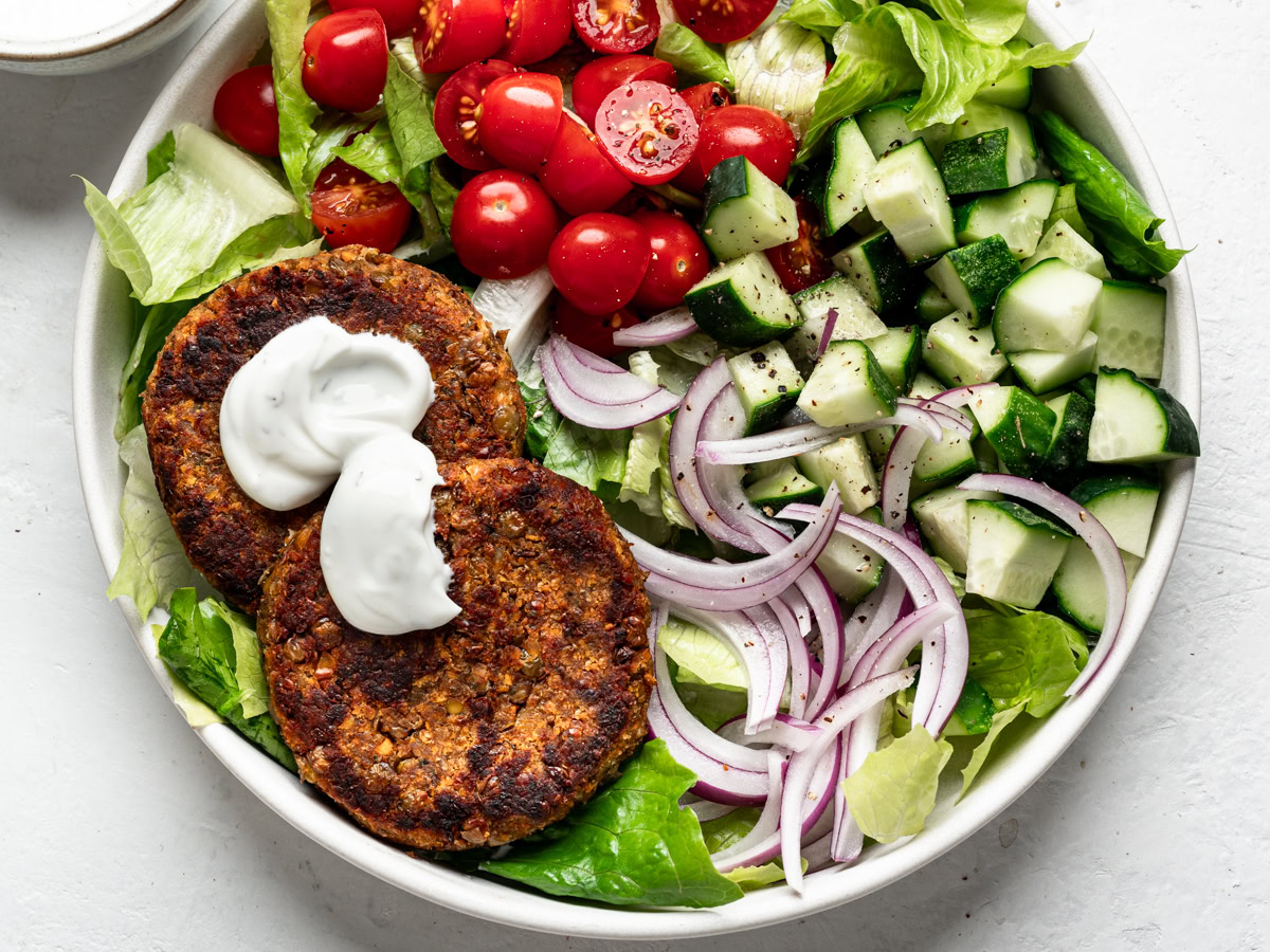 close up of plate with lentil patties on a bed of lettuce with tomatoes, onions and cucumbers