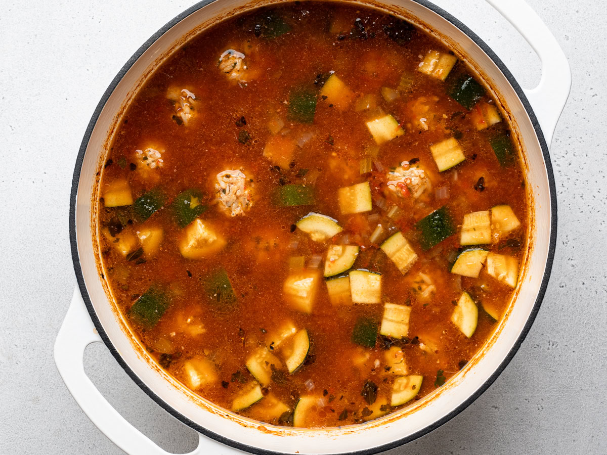 Cooked Albondigas soup in white Dutch oven with zucchini pieces floating on top