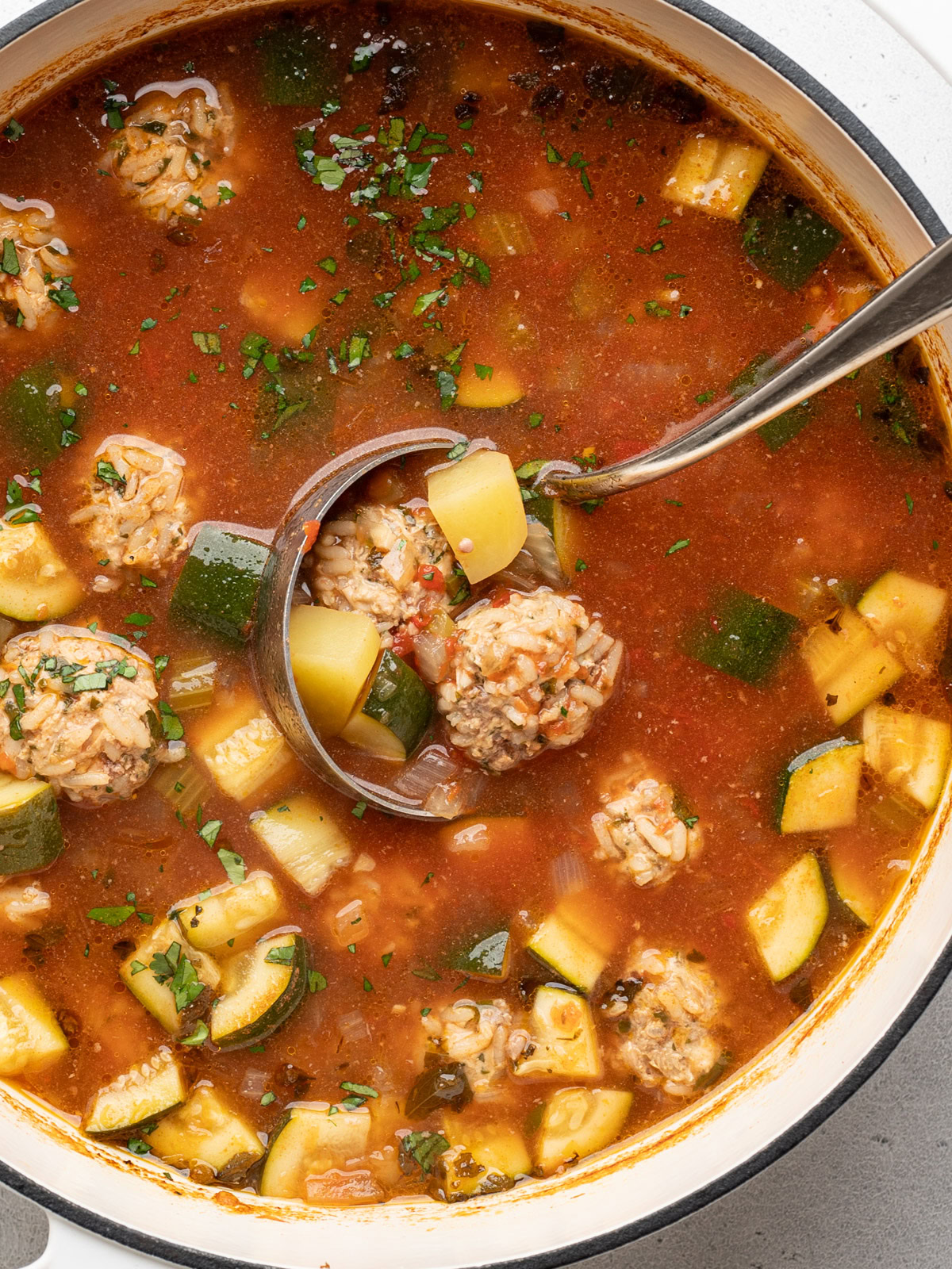 close up of ladle picking up cooked meatballs from broth