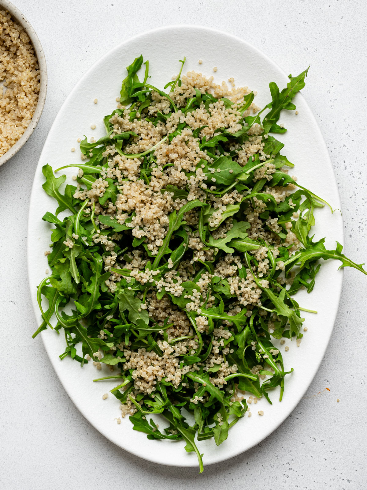 a white platter with a layer of arugula salad topped with cooked quinoa