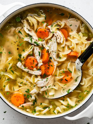 close-up of cooked turkey noodle soup in large white soup pot with a large spoon scooping out soup