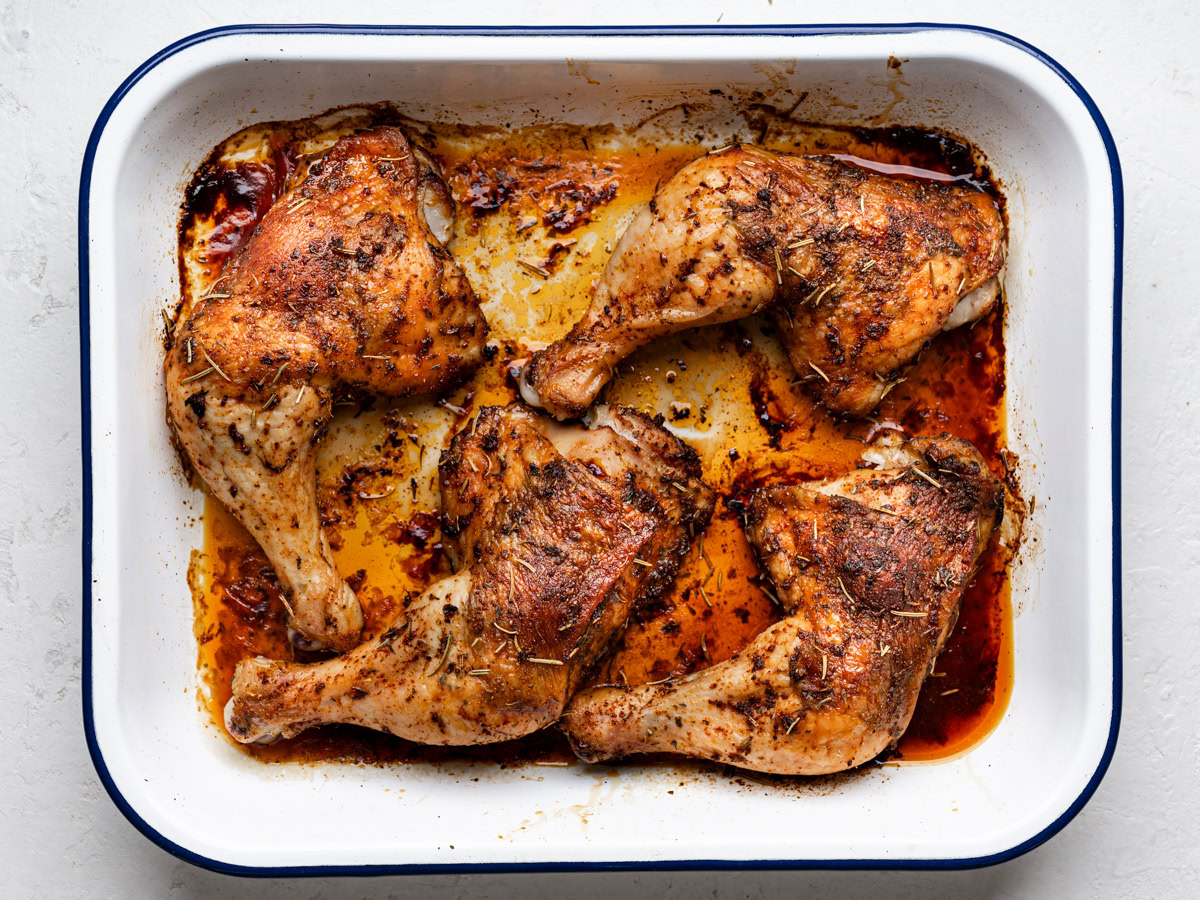 close up of baked chicken leg quarters on a white serving platter and garnished with fresh parsley  