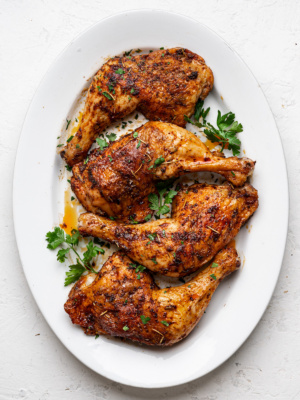 Four baked chicken leg quarters on a white platter garnished with fresh parsley