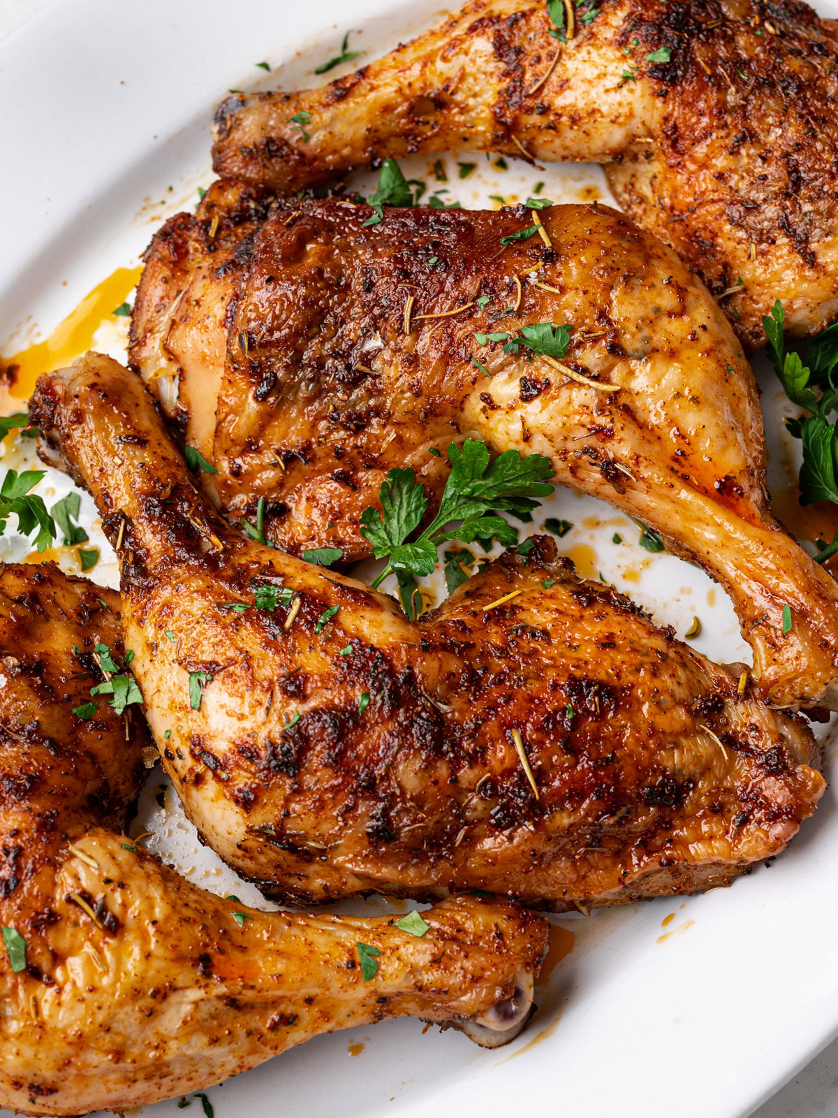 close up of baked chicken leg quarters on a white serving platter and garnished with fresh parsley  