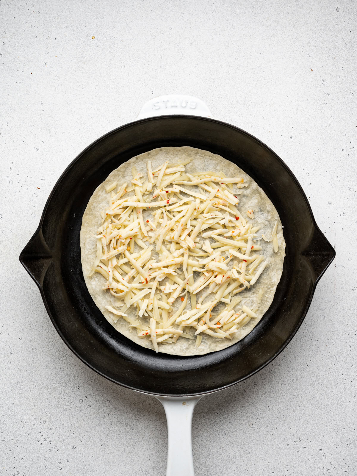 grated cheese sprinkled over tortilla in skillet