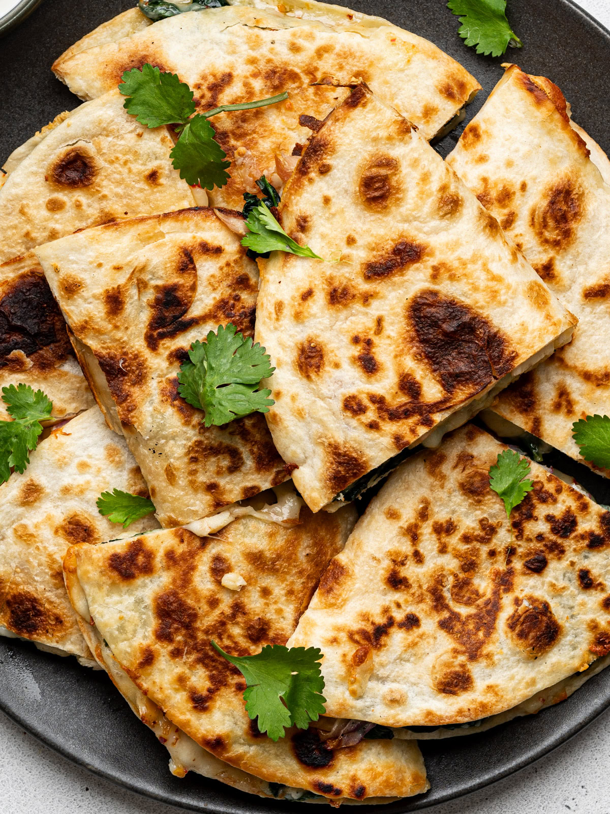 Close up of quesadilla triangles served on a black plate, garnished with cilantro