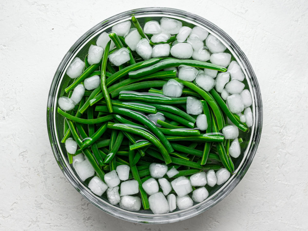 green beans in large glass bowl with water and ice (ice bath)