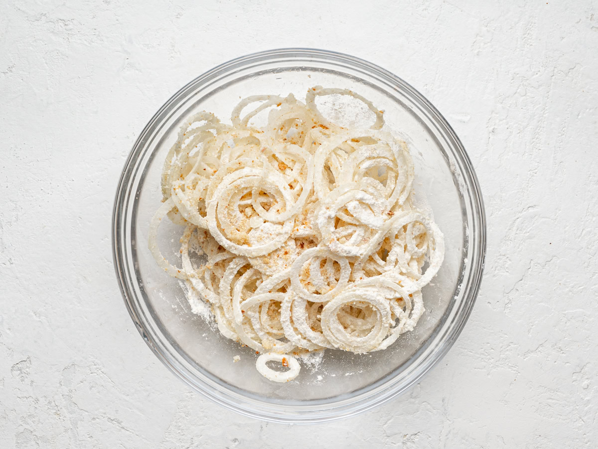 thinly sliced onions coated with flour in a glass bowl