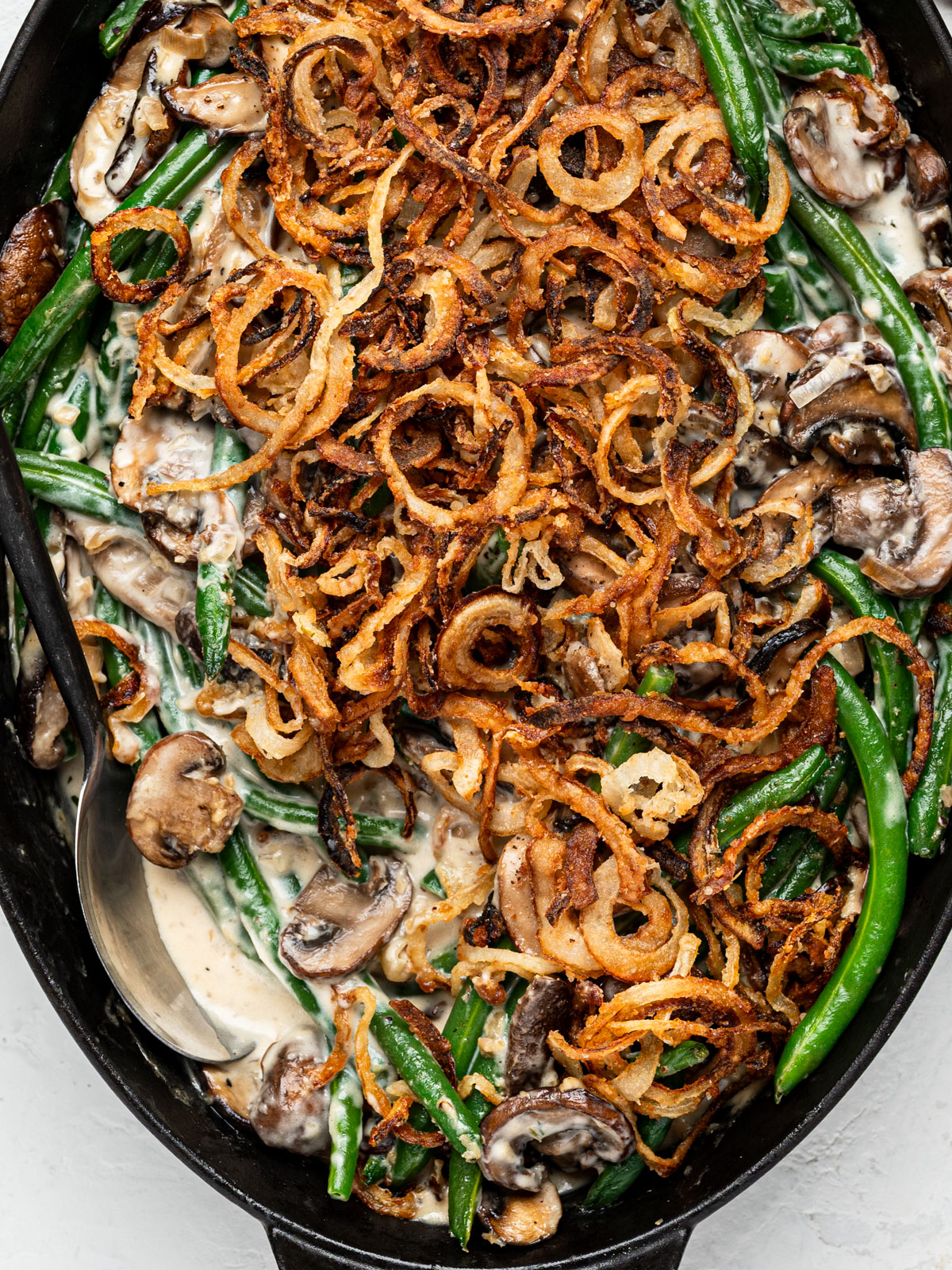 close up of baked green bean casserole in oval black baking dish with a serving spoon