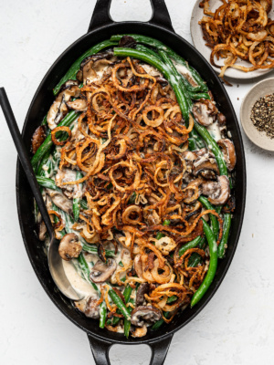 baked green bean casserole in oval black baking dish with crispy onions and black pepper in bowls on the side
