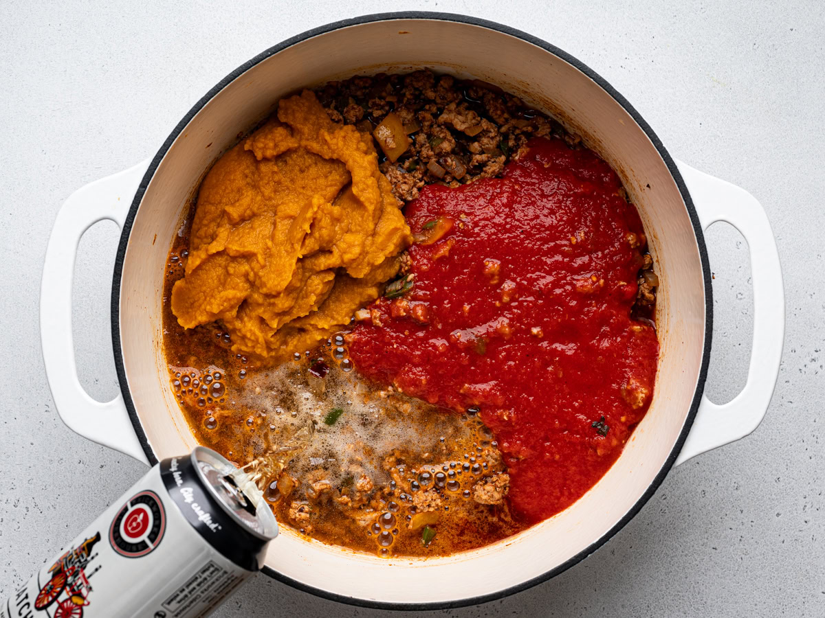 pouring beer into pot with turkey mixture, pumpkin puree and tomato sauce