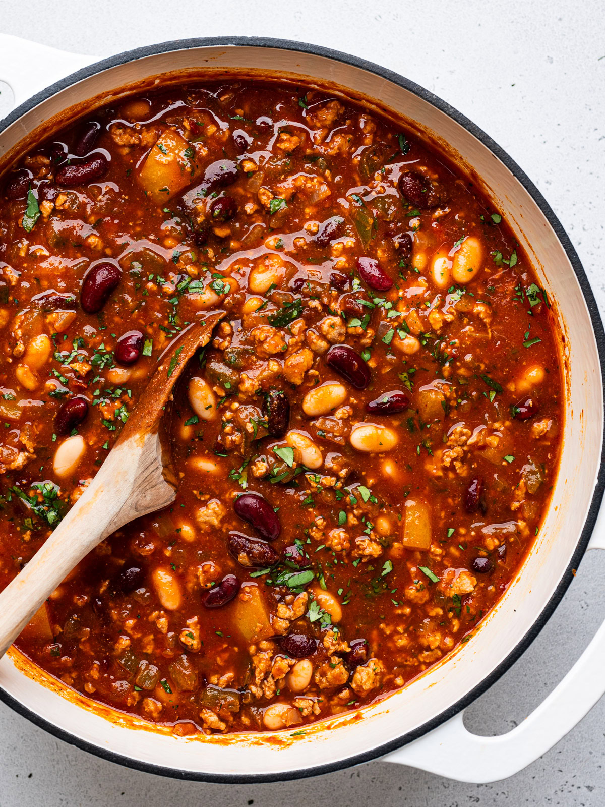 close-up of cooked chili in white pot with wooden spoon