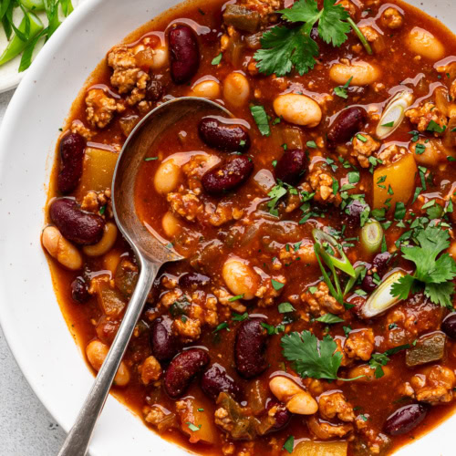 pumpkin chili served in white bowl and garnished with cilantro and green onions