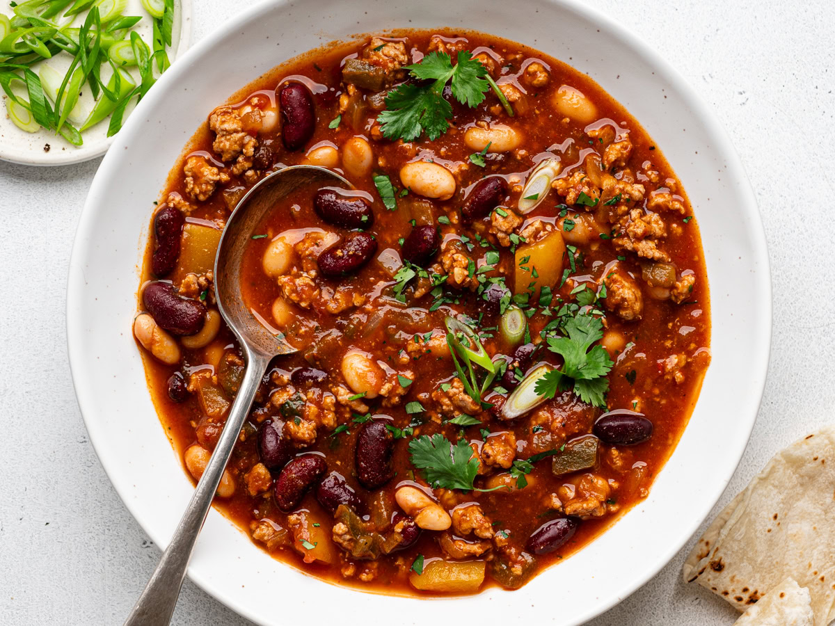 pumpkin chili served in white bowl and garnished with cilantro and green onions with charred tortilla pieces on the side