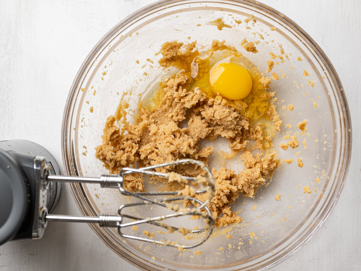 adding one egg to beaten butter and sugar mixture in glass bowl