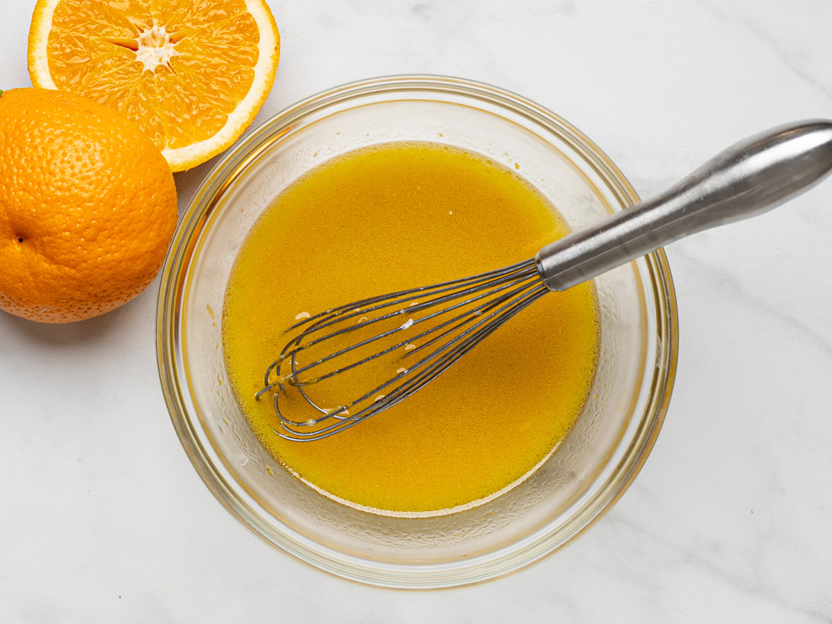 citrus dressing mixed in a glass bowl with orange halves on the side