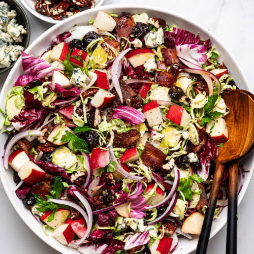 prepared winter Chopped Salad with citrus dressing in a large white bowl with pecans and blue cheese in small bowls on the side