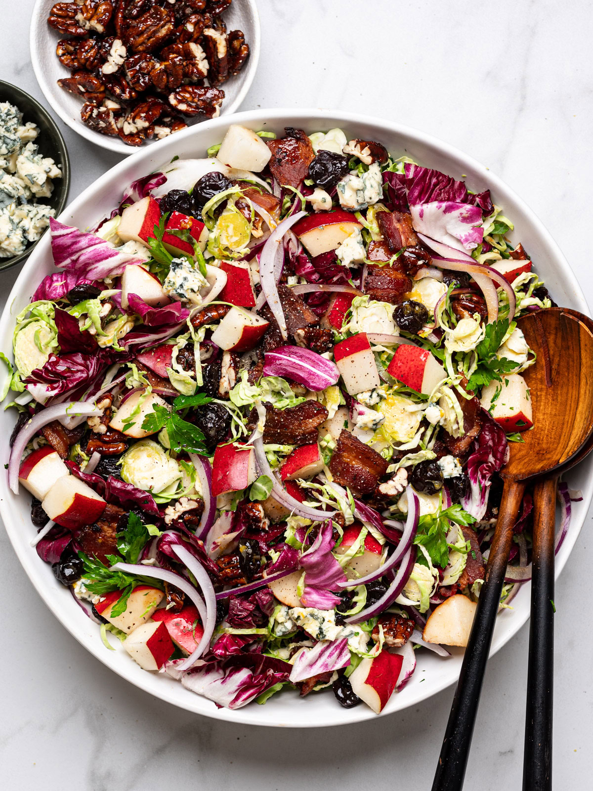 prepared winter Chopped Salad with citrus dressing  in a large white bowl with pecans and blue cheese in small bowls on the side