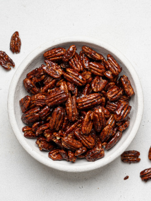 candied pecans served in white bowl with a few pecans fallen on the background
