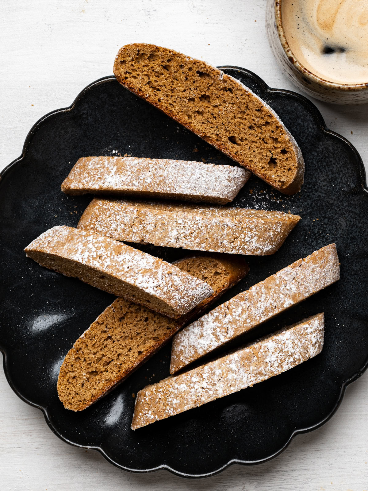 a few biscotti served on a black plate with a mug of coffee on the side