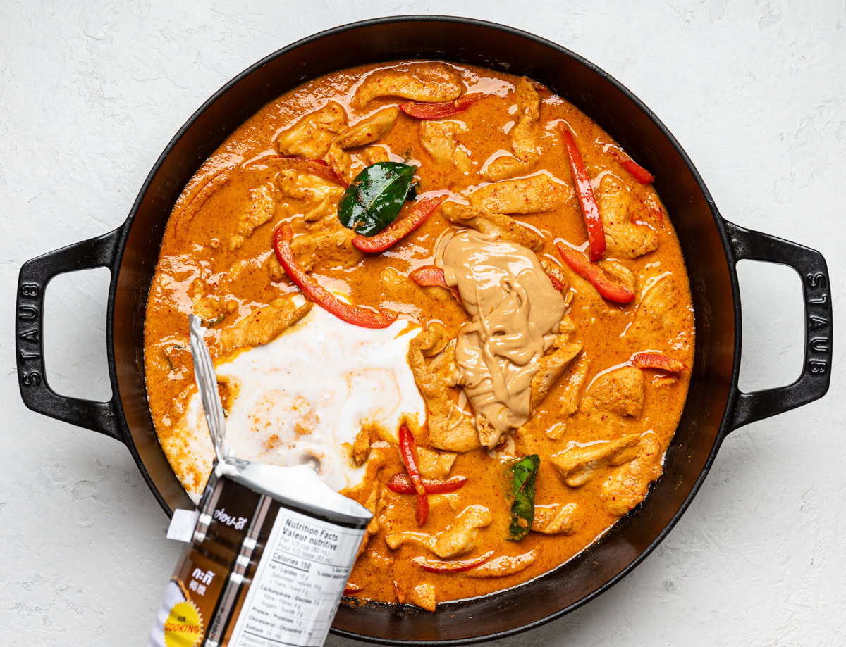 adding peanut butter and coconut milk to skillet with chicken and sauce