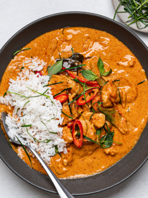Panang chicken curry in a black bowl topped with white rice on one side