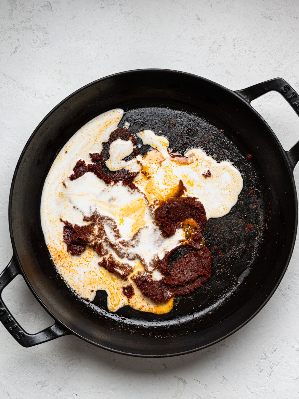 adding coconut milk to curry paste in skillet