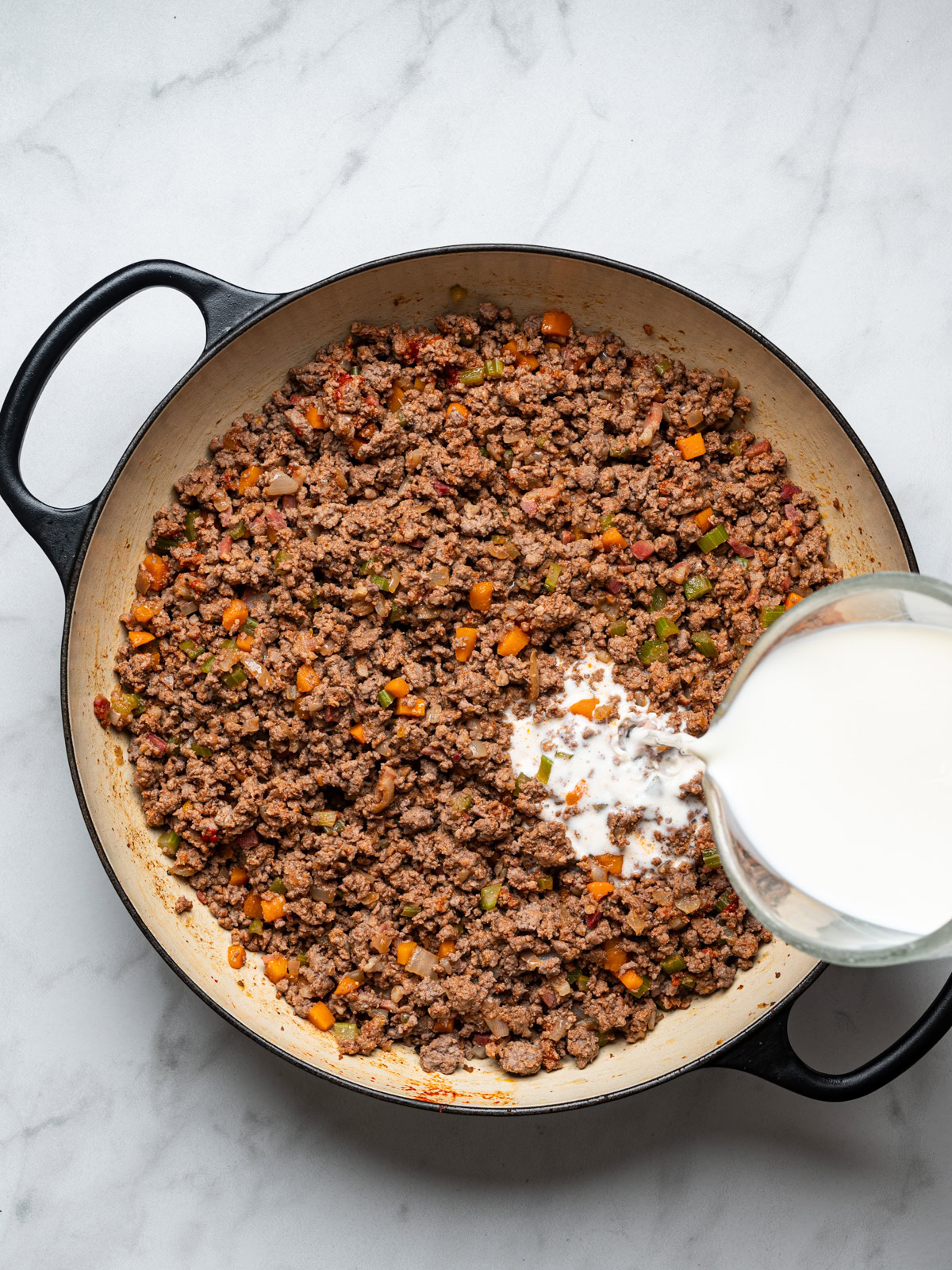 adding milk to browned meat mixture in skillet