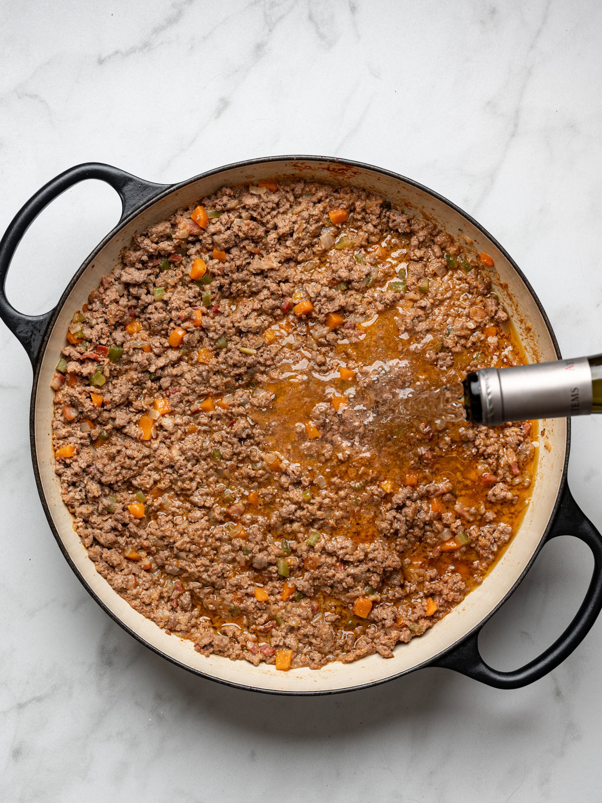 adding wine to browned meat mixture in skillet