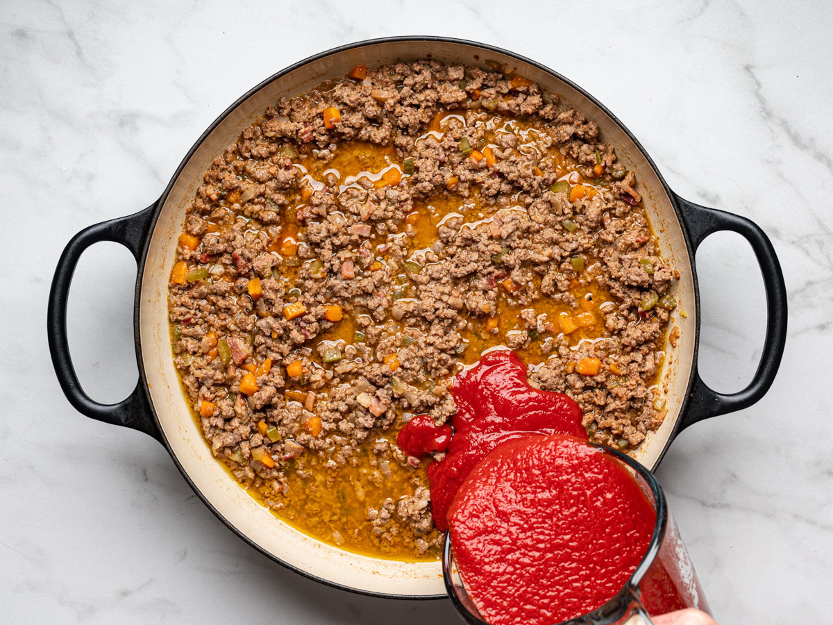 adding passata to meat mixture in skillet