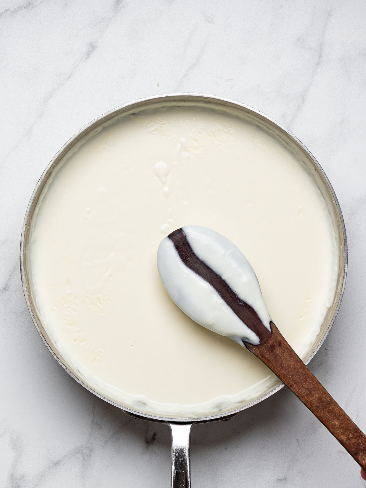 back of a wooden spoon showing bechamel sauce has thickened