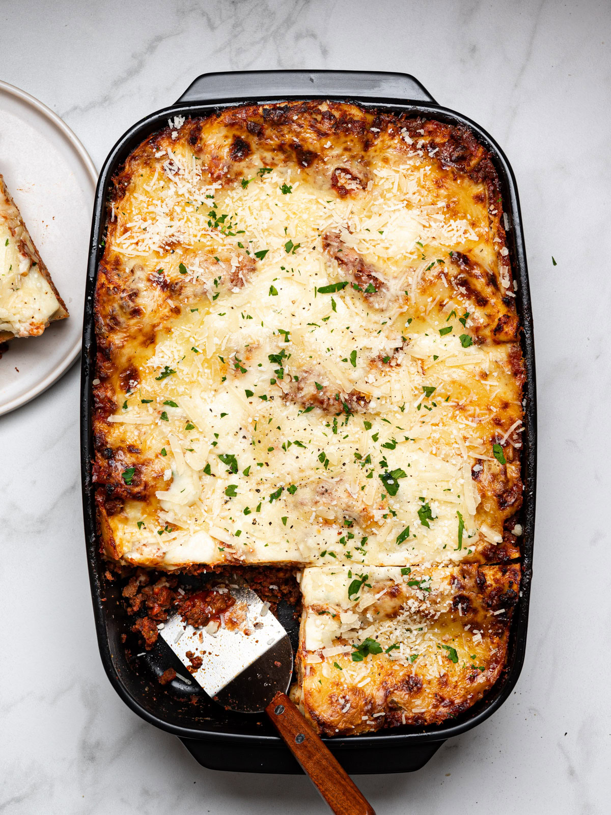 baked lasagna al forno in a black baking dish with one slice cut out and served