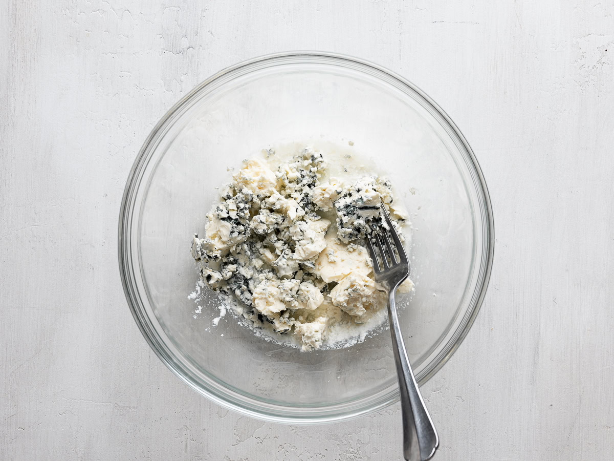 mashing blue cheese with milk mixture in glass bowl