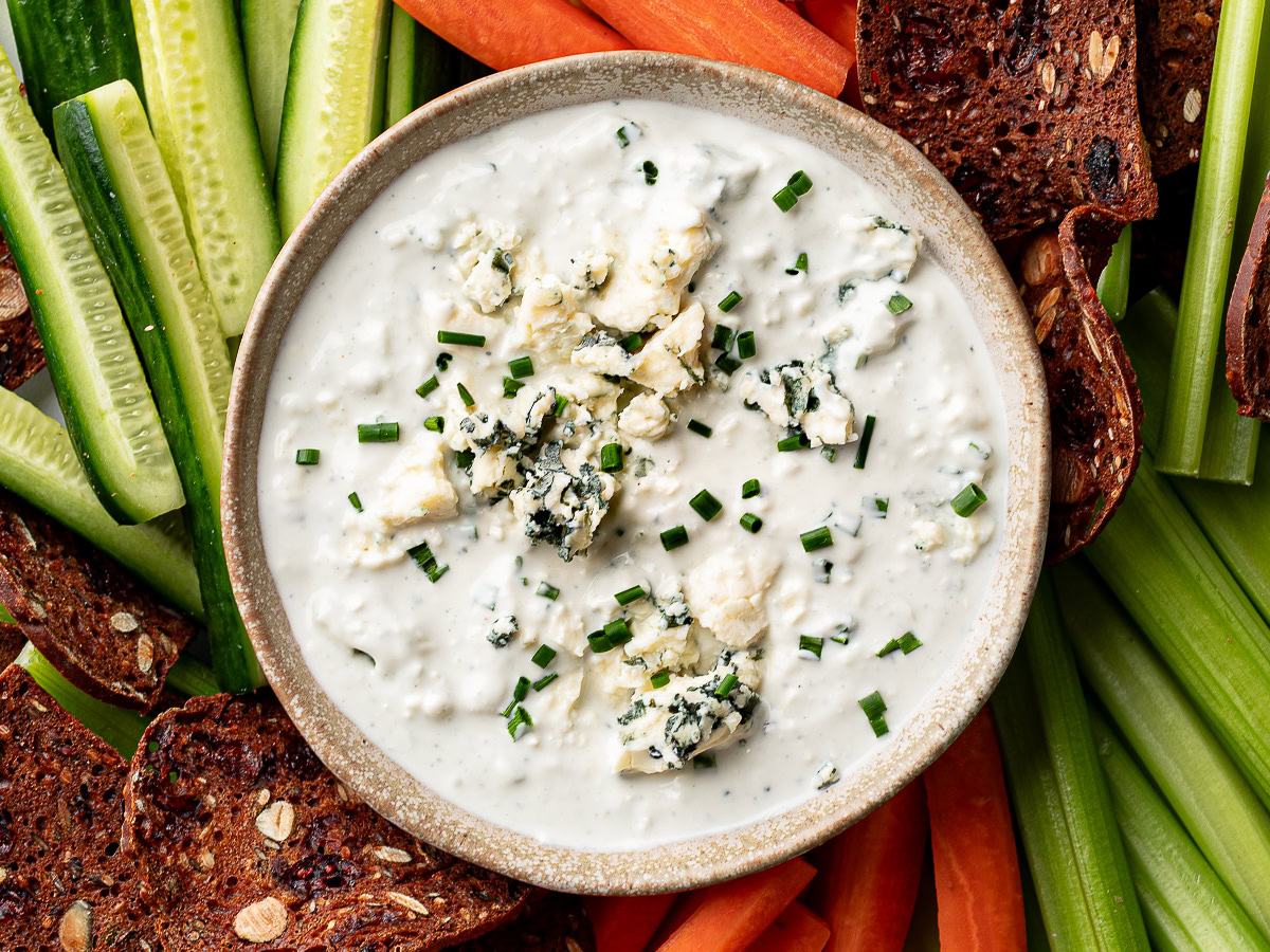 blue cheese dip in bowl with raw veggies and crackers around it