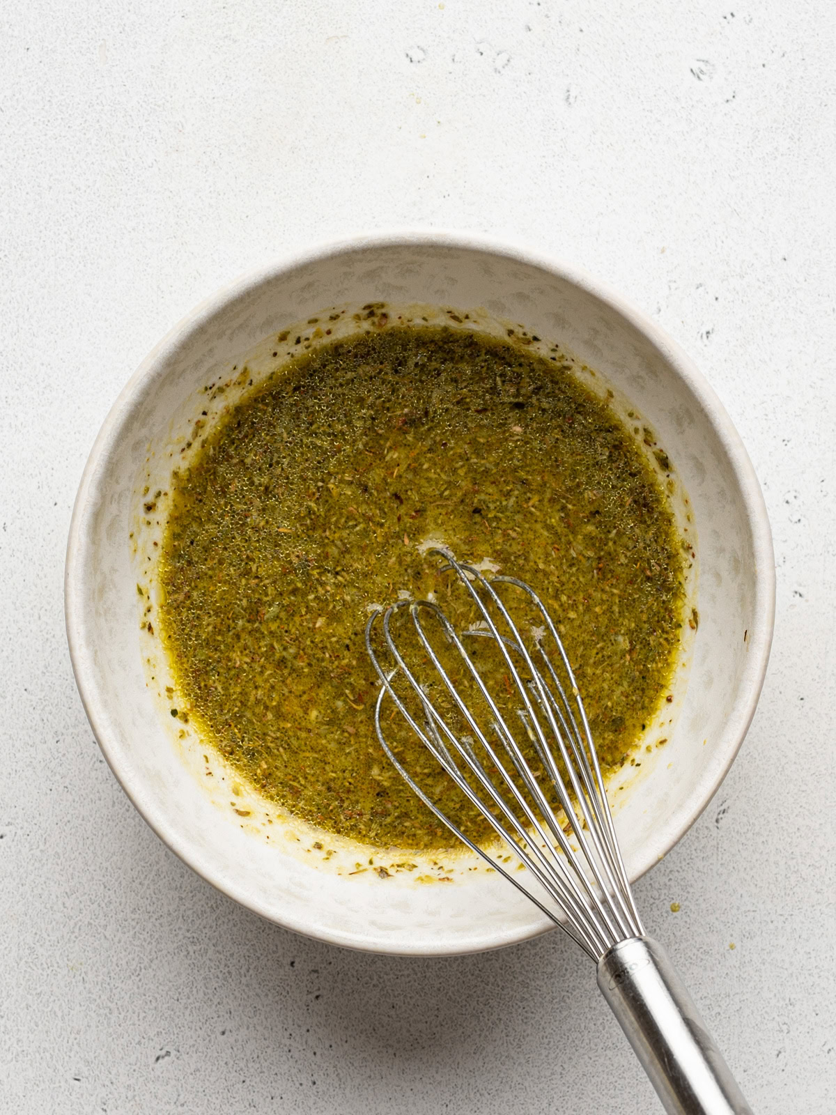 Mixed marinade in white bowl with a whisk