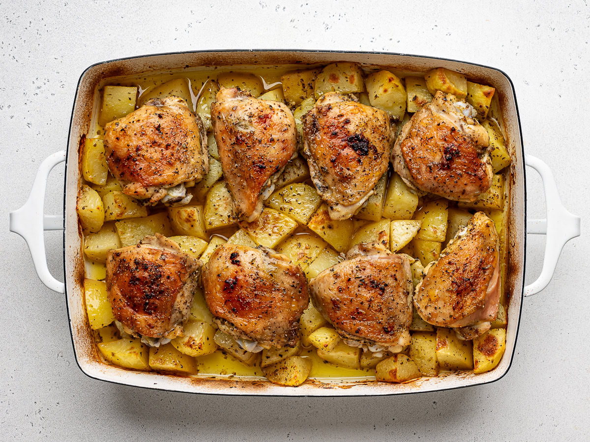 Baked Greek chicken and potatoes just out of the oven in white casserole dish with no garnishes