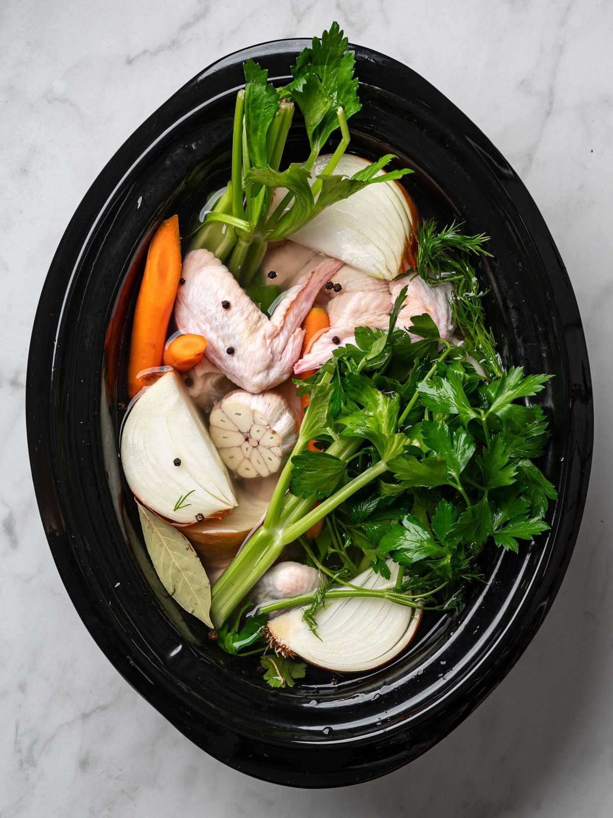 raw chicken bones and vegetables in slow cooker insert filled with water