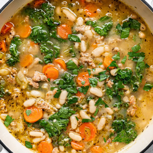 closeup of kale and white bean sausage soup in large soup pot and garnished with chopped parsley