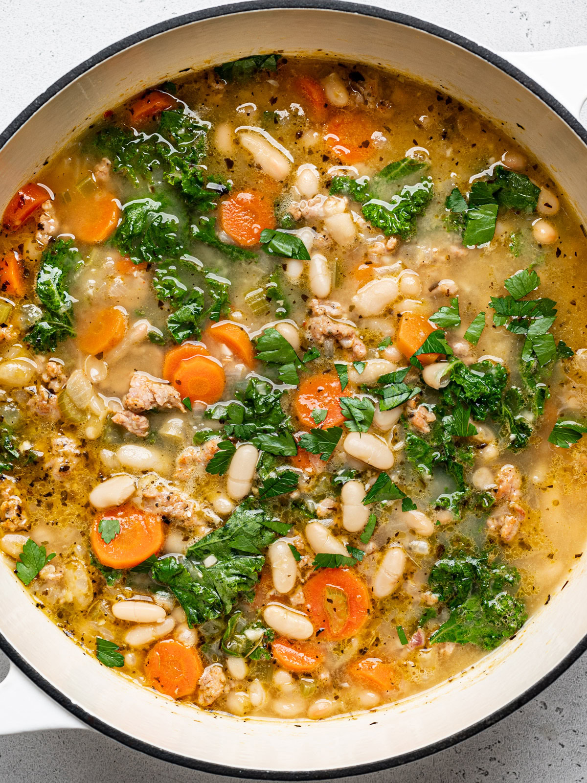 closeup of kale and white bean sausage soup in large soup pot and garnished with chopped parsley