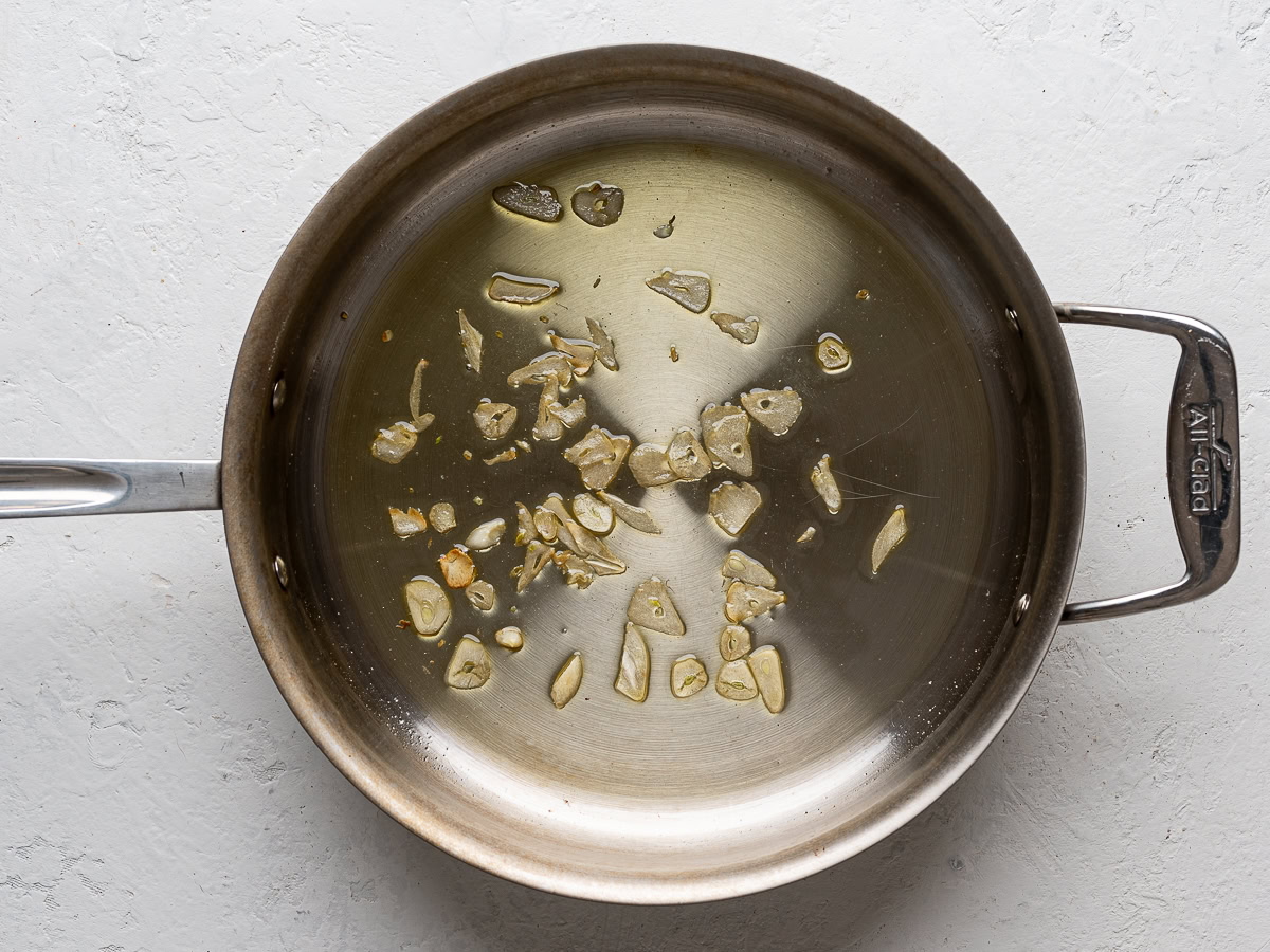 sliced garlic cooking in a large stainless steel skillet