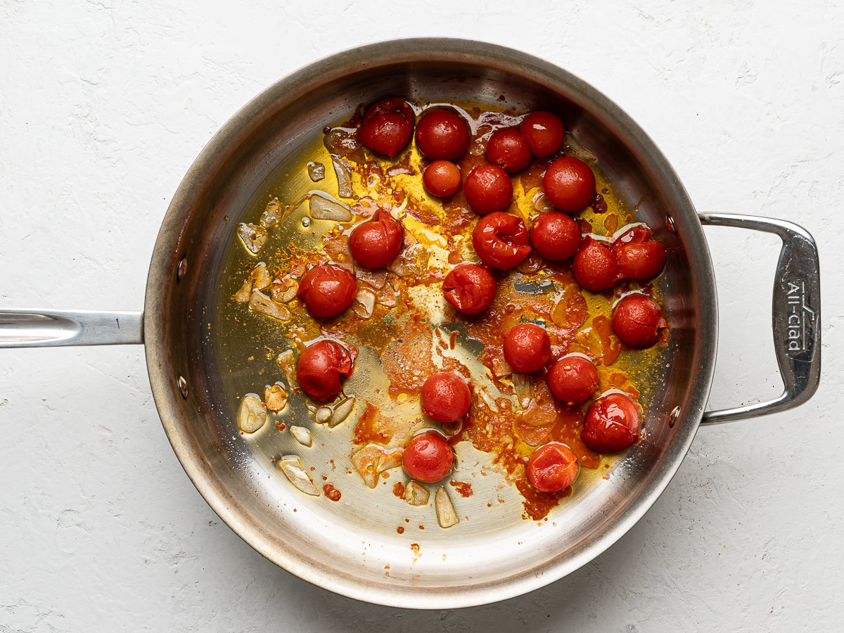 cherry tomatoes cooking with garlic in large stainless steel pan