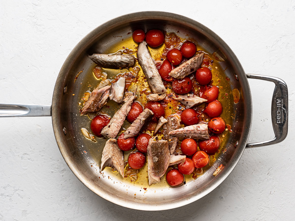 mackerel fillets cooking with cherry tomatoes and garlic in large stainless steel pan