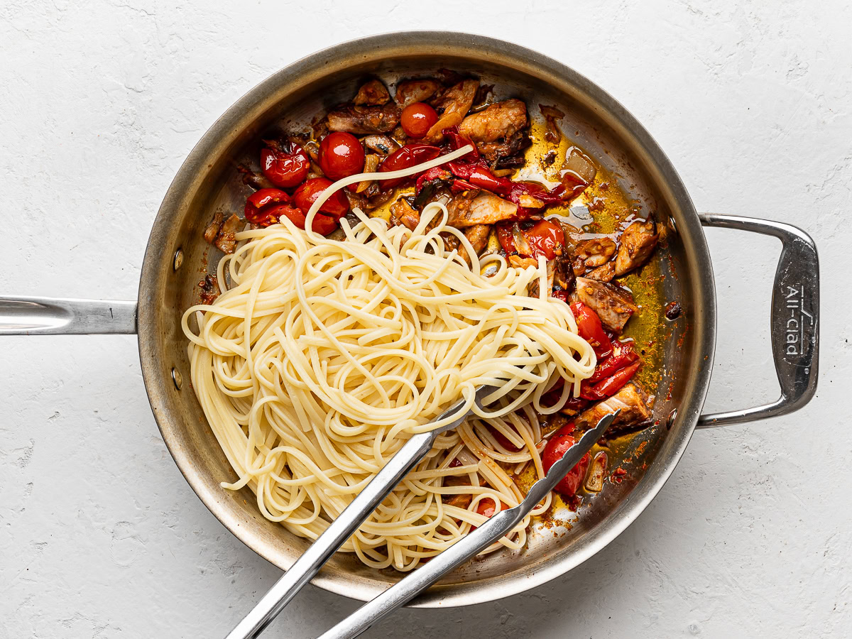 cooked spaghetti added to mackerel sauce mixture in large stainless steel pan