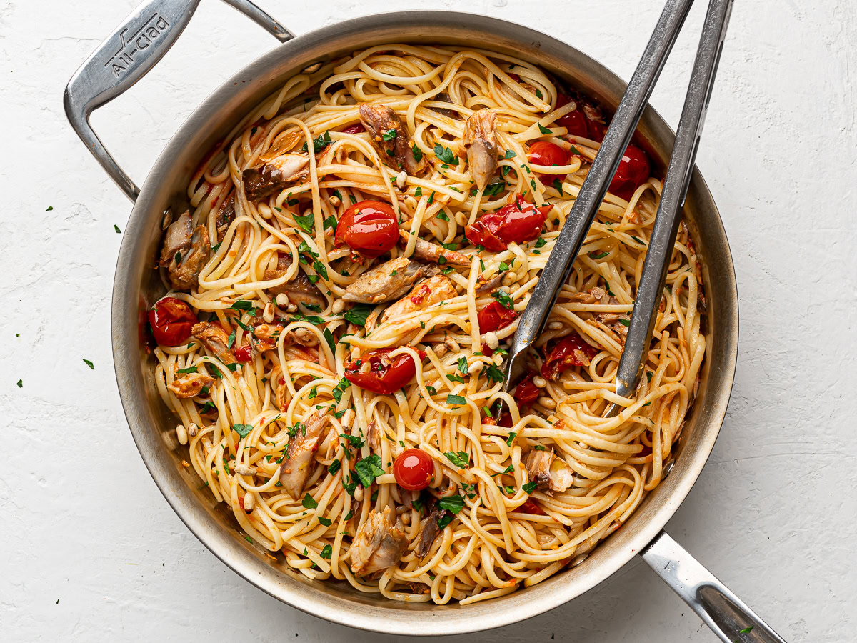 mackerel pasta mixture in large stainless steel pan garnished with pine nuts and chopped parsley