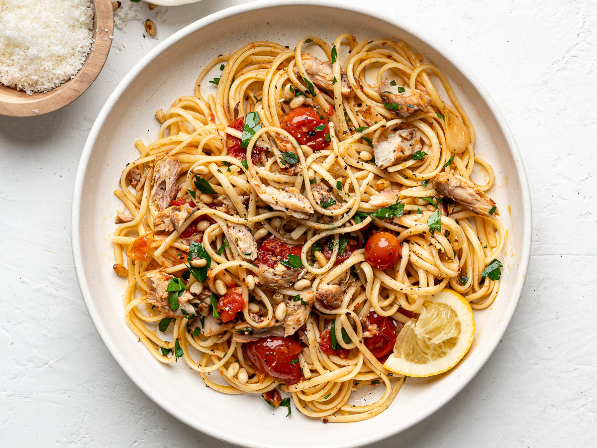 canned mackerel pasta served on white plate with bowl of parmesan on the side
