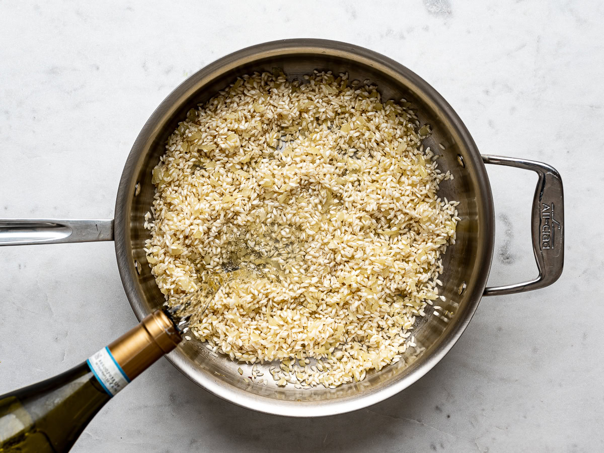 arborio rice toasted with the onions in a large stainless steel skillet and wine getting poured in from a bottle